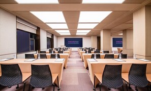 A conference room with multiple tables and chairs, a large screen displaying 'Intercity Hotel' branding, and a modern ceiling design.