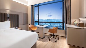 A hotel room with a large window, a bed, a desk, two chairs, and a minibar. - Intercity Hotel Shanghai Hongqiao Airport (Shanghai)