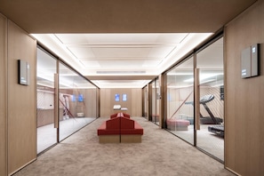 Ein modernes Interieur mit einer zentralen roten Sitzecke, Glaswänden und einem im Hintergrund sichtbaren Fitnessbereich.
