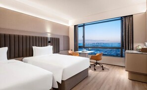 Habitación de hotel con dos camas, un escritorio, una silla y un ventanal con vistas a la ciudad.