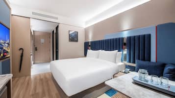 A modern hotel room with a large bed, a desk with a phone and glasses, and a TV on the left.