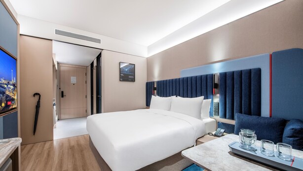 A modern hotel room with a large bed, a desk with a phone and glasses, and a TV on the left. - Intercity Hotel Shanghai Hongqiao Airport (Shanghai)