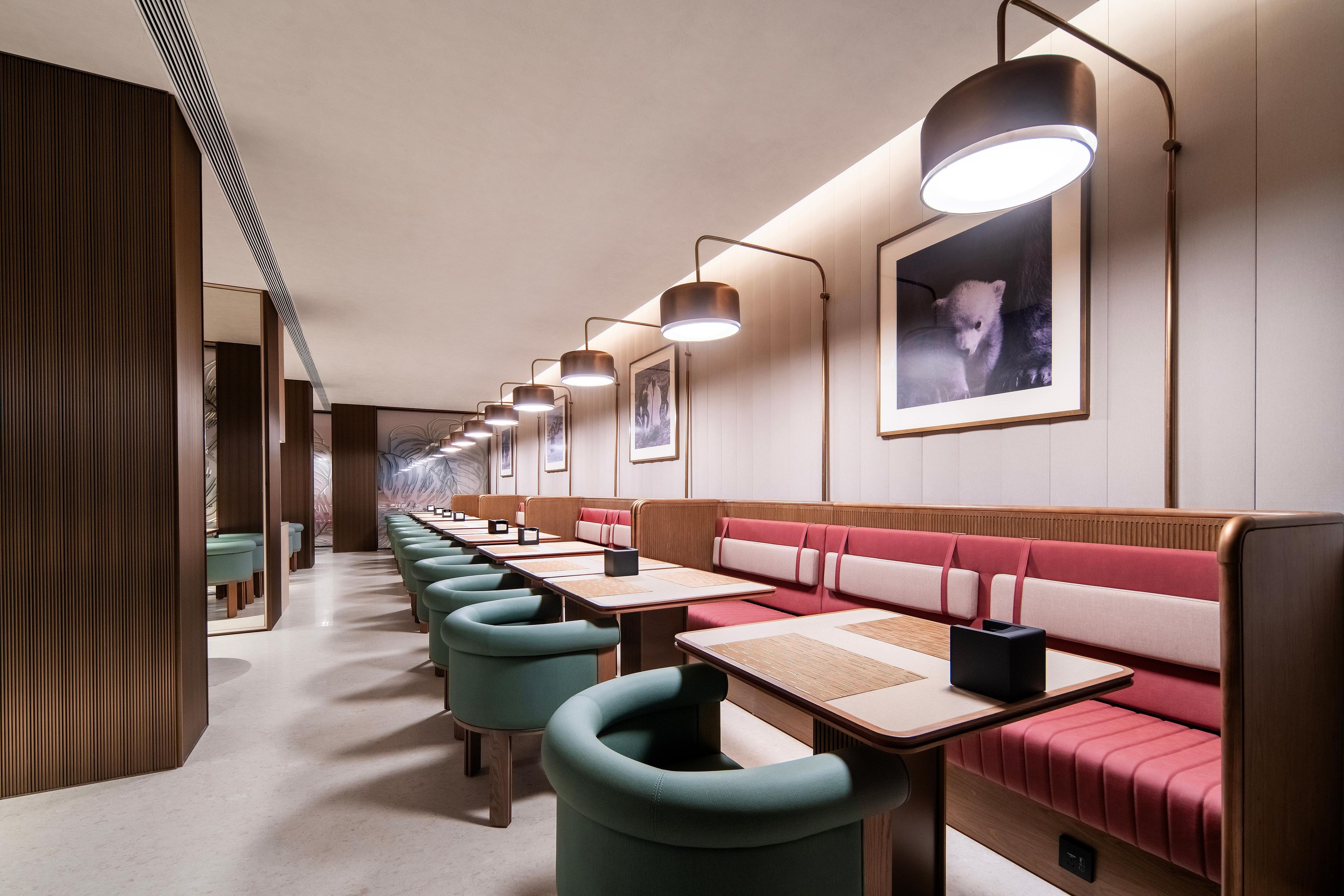 Une rangée de chaises turquoise et de tables en bois dans un restaurant avec des banquettes rouges rembourrées et des tableaux encadrés accrochés au mur.