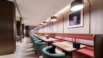 Une rangée de chaises turquoise et de tables en bois dans un restaurant avec des banquettes rouges rembourrées et des tableaux encadrés accrochés au mur.