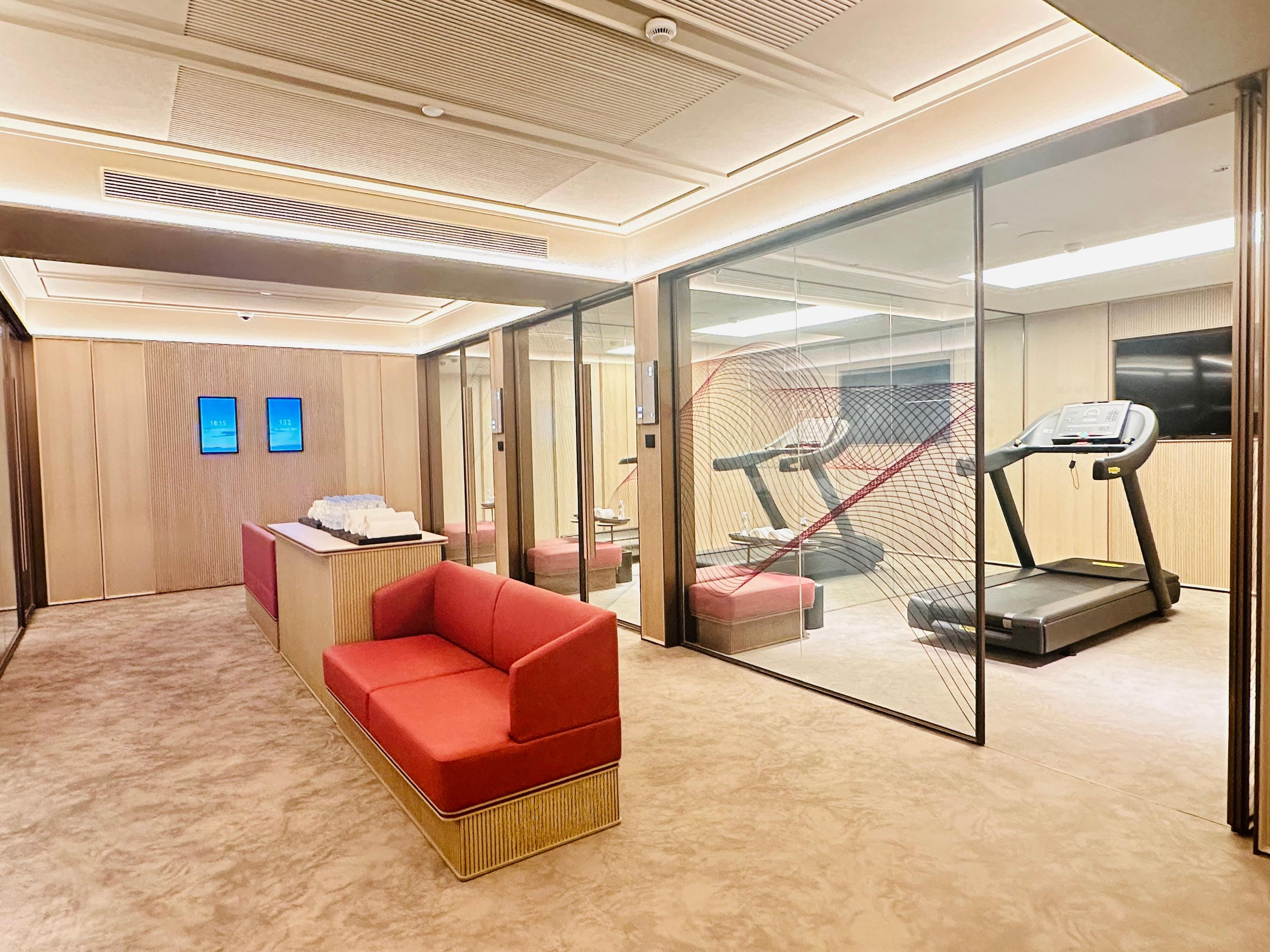 Moderni hotellihuone, jossa on punainen sohva, juoksumatto ja lasiseinä.