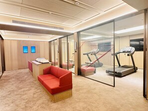 Moderni hotellihuone, jossa on punainen sohva, juoksumatto ja lasiseinä.