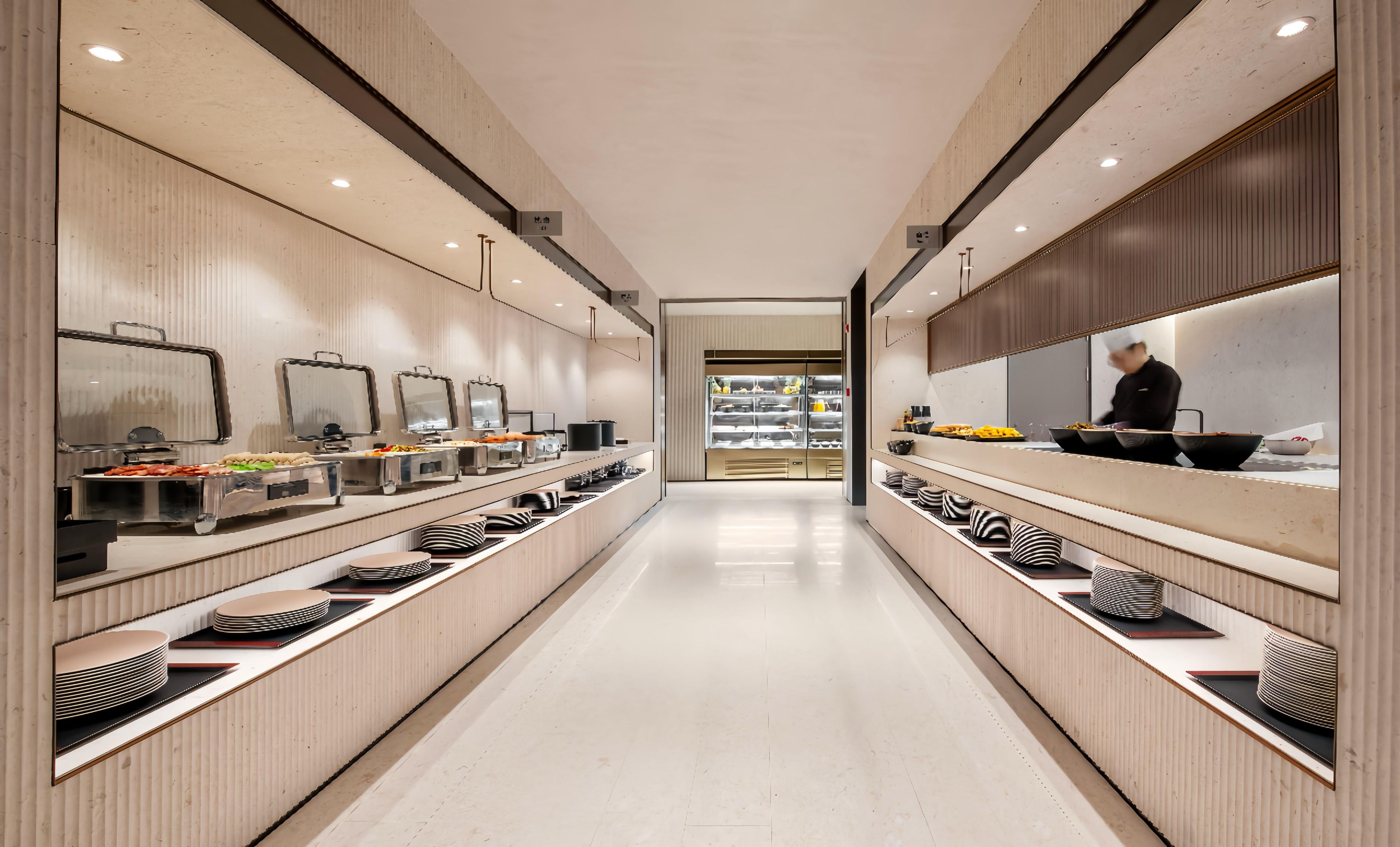 Un pasillo moderno y bien iluminado con una zona de bufé a ambos lados, que presenta exhibiciones de alimentos ordenadas y un área de cocina visible.