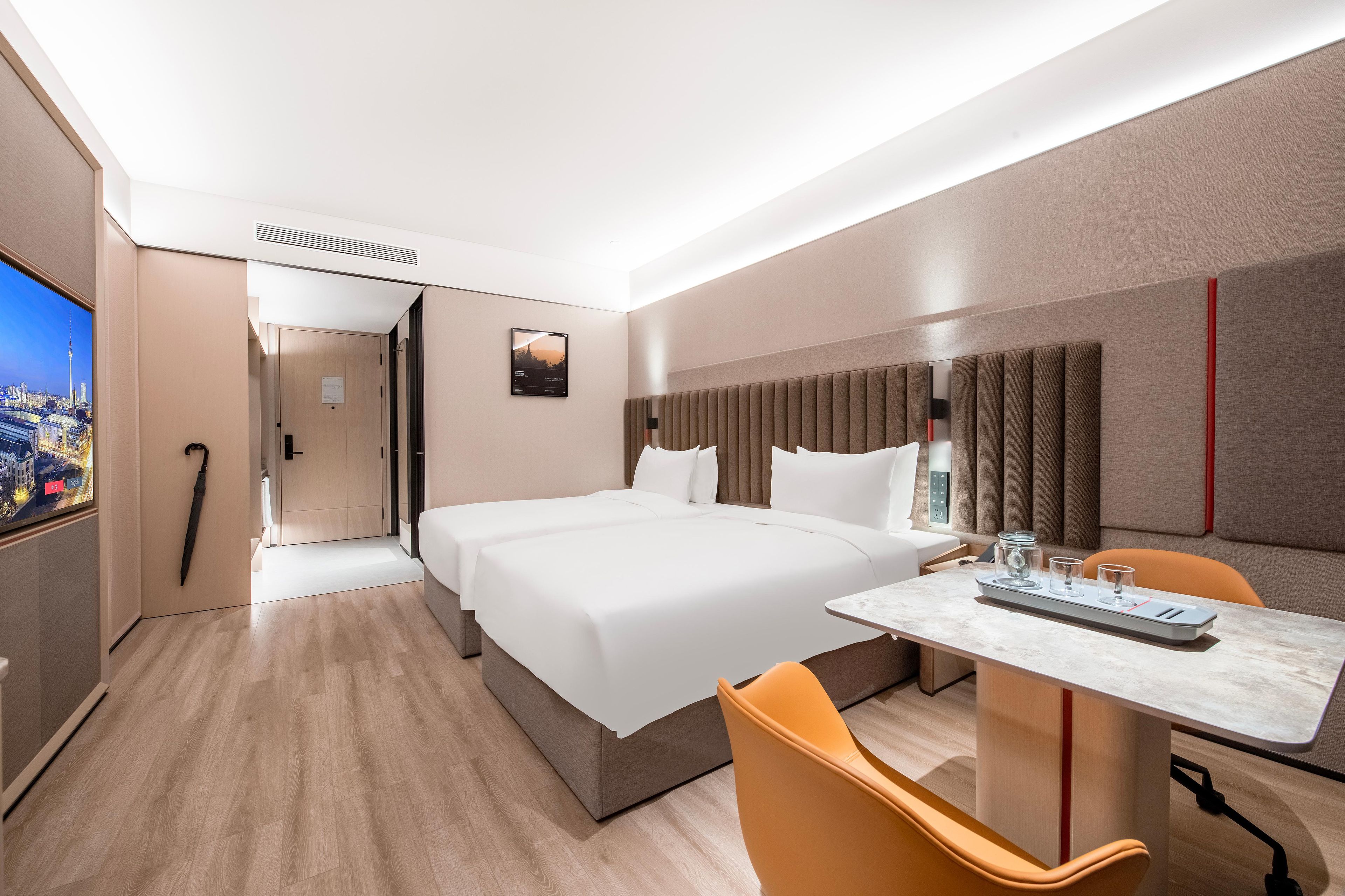 A hotel room with a large bed, a desk with a chair, a TV, and a cityscape view.