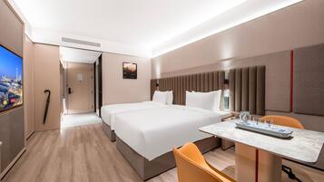 Habitación de hotel con una cama grande, un escritorio con silla, televisión y vista a la ciudad.