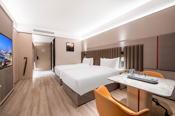 A hotel room with a large bed, a desk with a chair, a TV, and a cityscape view.