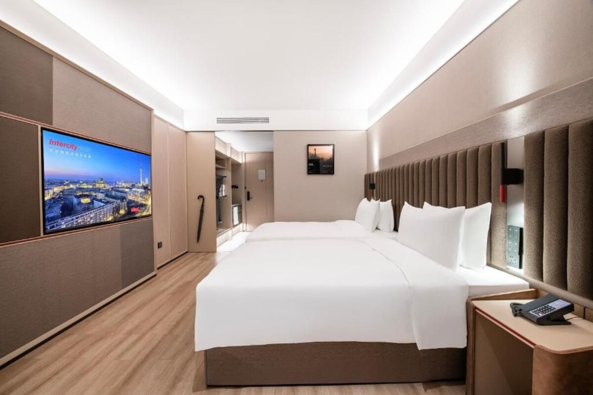 A hotel room with a large bed, a TV on the wall, and a bedside table with a phone.