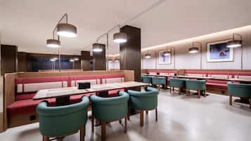 Interior moderno de restaurante, com cabines e mesas, iluminação pendente e quadros nas paredes.