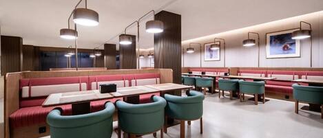 A modern restaurant interior with booths and tables, pendant lighting, and framed artwork on the walls.