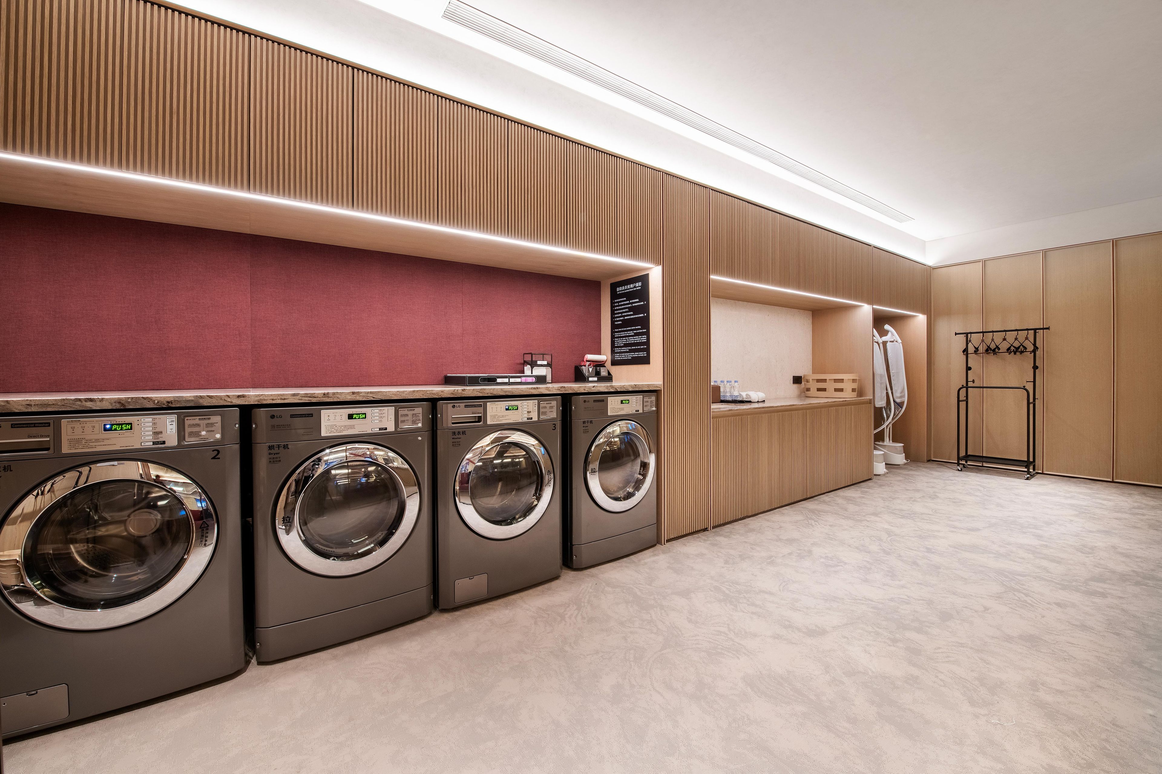 A modern laundry room with four front-loading washing machines, a drying rack, and a wall-mounted ironing station.