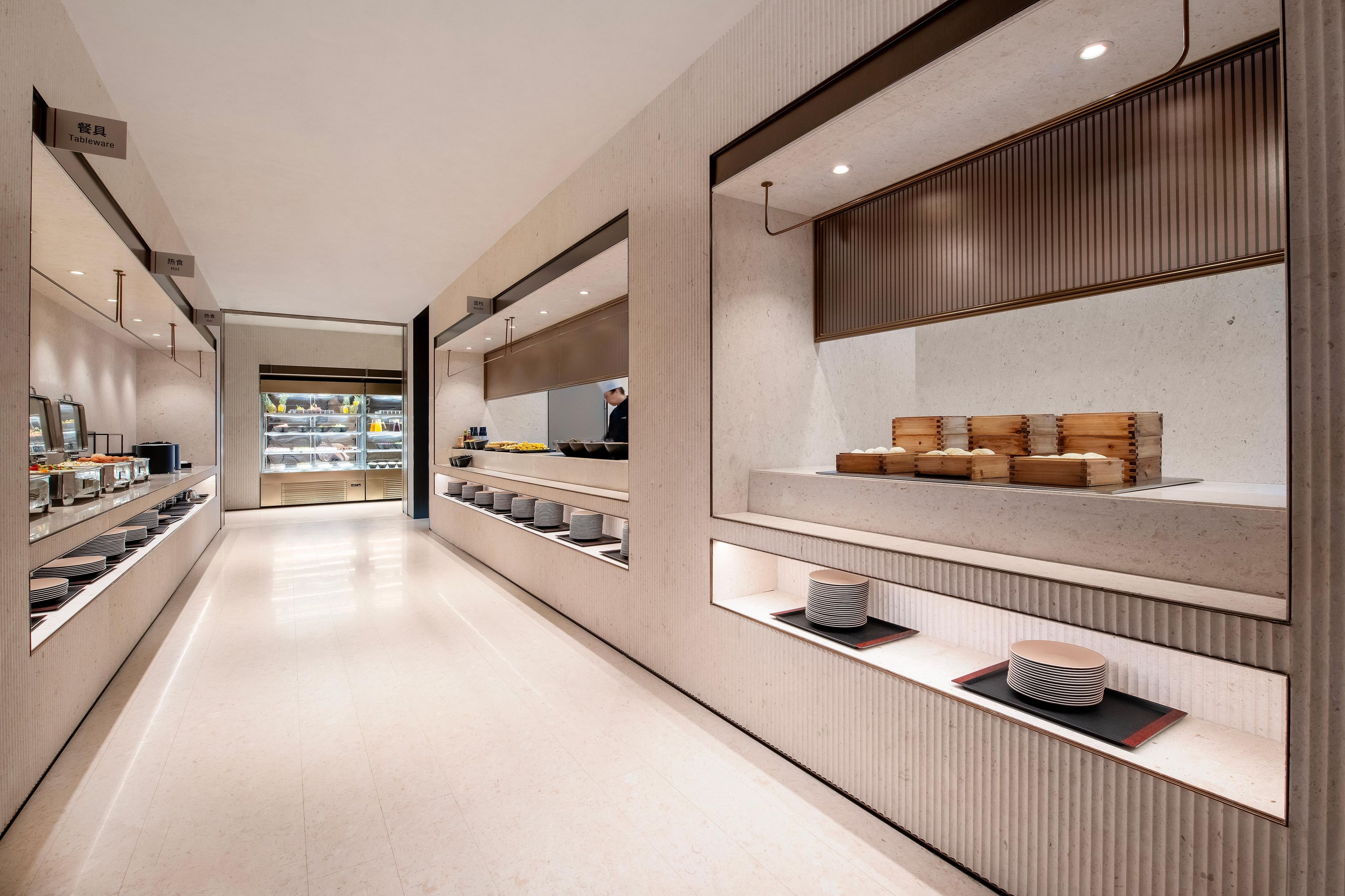A modern, well-lit corridor with display shelves on both sides, leading to a counter area.