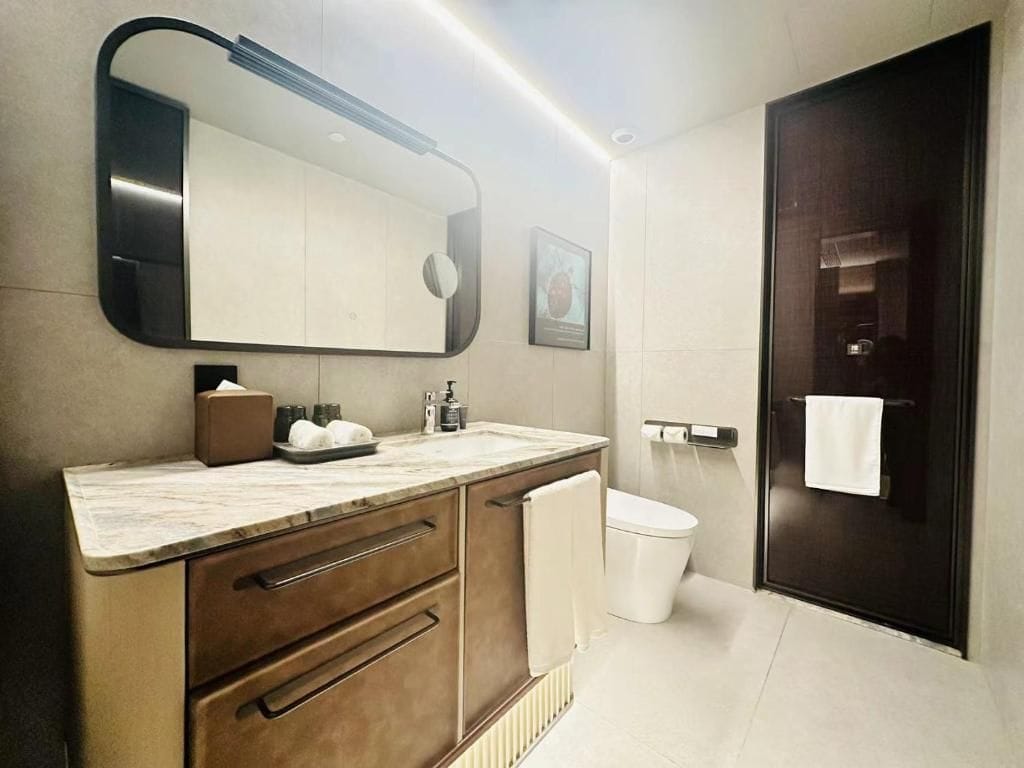 A modern bathroom with a large mirror, a marble countertop, a white toilet, and a dark door.