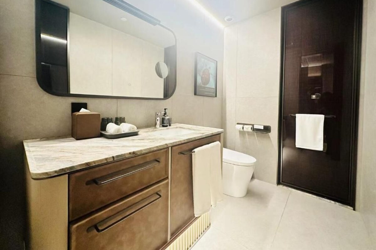 A modern bathroom with a large mirror, a marble countertop, a white toilet, and a dark door.