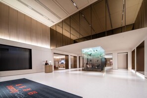 A spacious lobby with a reception desk, a glass wall with a bird mural, and a large digital screen.