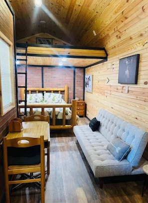 Cozy cabin room with a comfortable sofa, dining table, and wooden paneling.