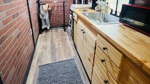 A narrow kitchen with wooden cabinets, a brick wall, and a small countertop. - Lovely Little Cabin in the Woods (Ocklawaha)