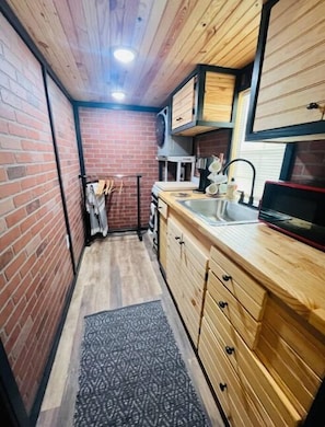 Compact kitchen with exposed brick walls, wooden cabinetry, and a small countertop.