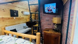 A cozy room with a bed, a sofa, a TV, and a small wooden cabinet. - Lovely Little Cabin in the Woods (Ocklawaha)