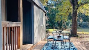 A wooden deck with a table and chairs, a metal railing, and a building with a corrugated metal roof. - Lovely Little Cabin in the Woods (Ocklawaha)