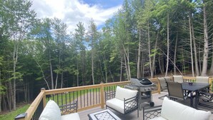 Eine Terrasse mit Gartenmöbeln, einem Grill und Blick auf einen Wald.