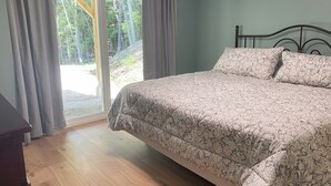 Ein Schlafzimmer mit Bett, Holzboden und Blick auf einen Wald durch eine Glasschiebetür.