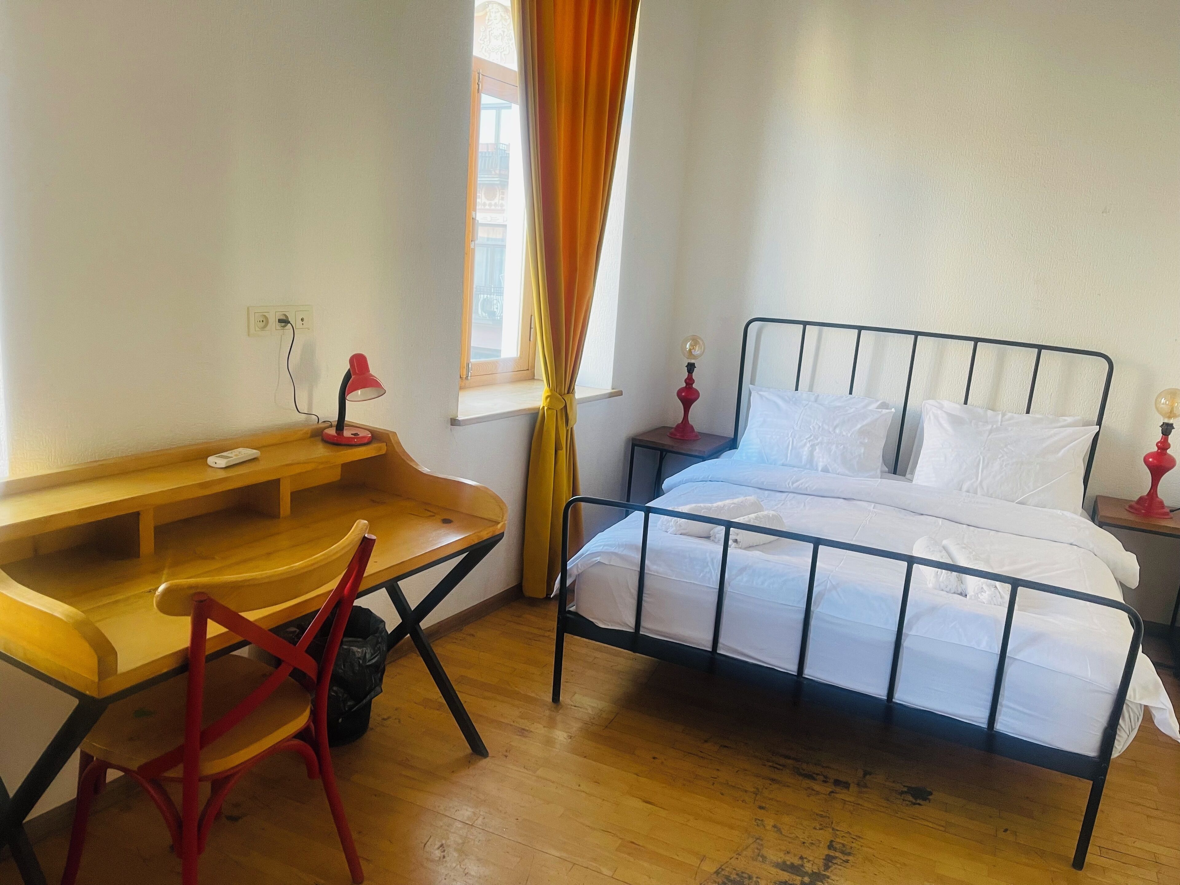 Un dormitorio con un escritorio de madera, una cama con ropa blanca y dos lámparas de noche.