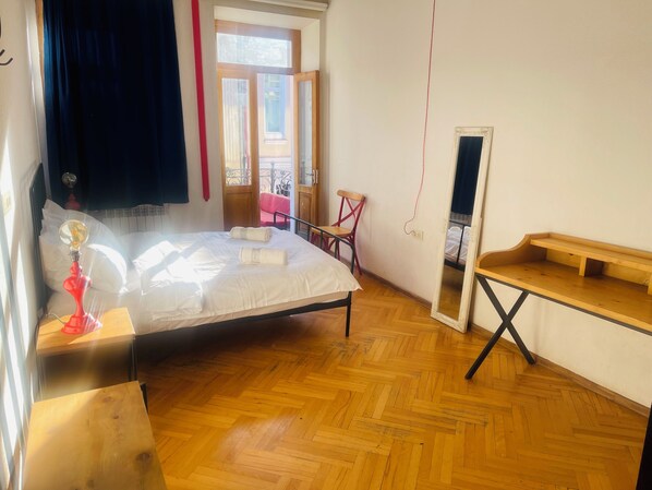 Un dormitorio con cama, una silla de madera, una mesita, un espejo y vistas al balcón.
