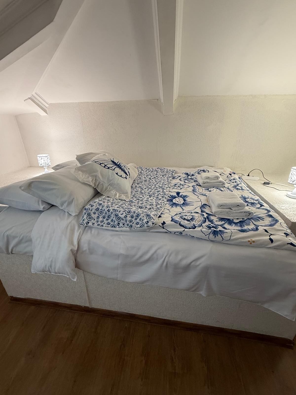 A neatly made bed with floral bedding and pillows, a bedside lamp, and a power outlet on the nightstand.