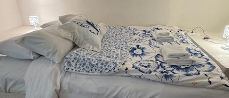 A neatly made bed with floral bedding and pillows, a bedside lamp, and a power outlet on the nightstand.