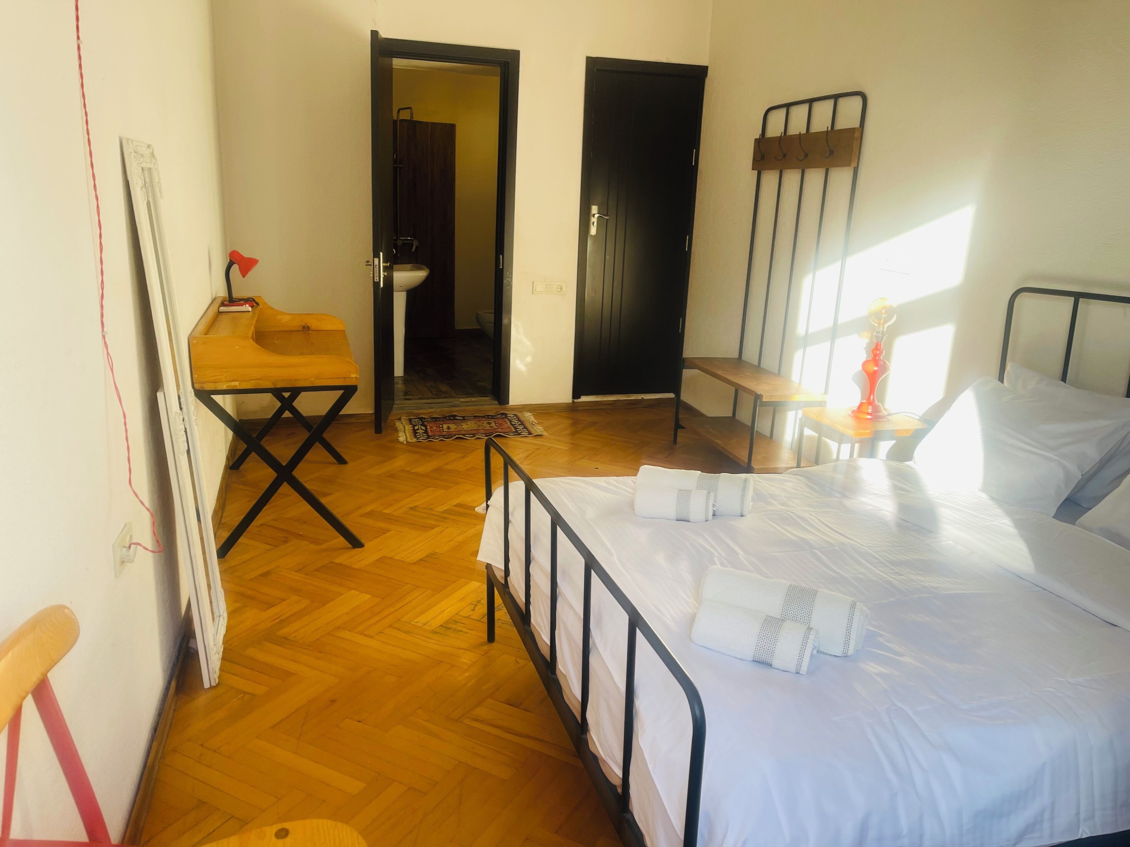 A bedroom with a bed, a small table with a lamp, a chair, and a wooden bench.