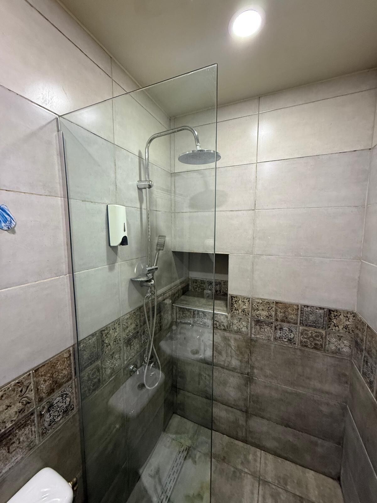 A shower area with a glass partition, a handheld showerhead, and a soap dispenser on the wall.