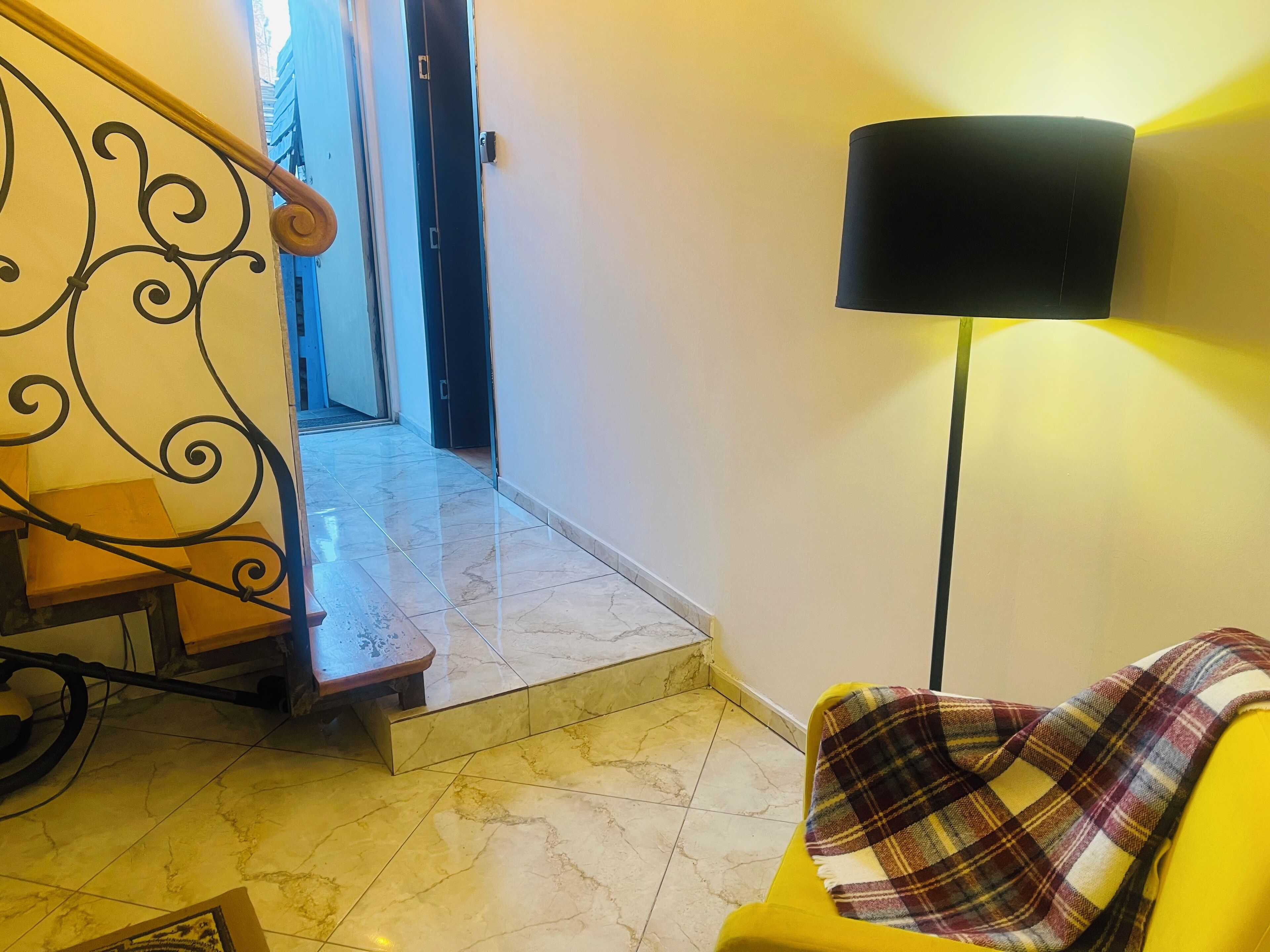 A staircase with a metal railing, a yellow chair with a plaid blanket, and a black floor lamp.