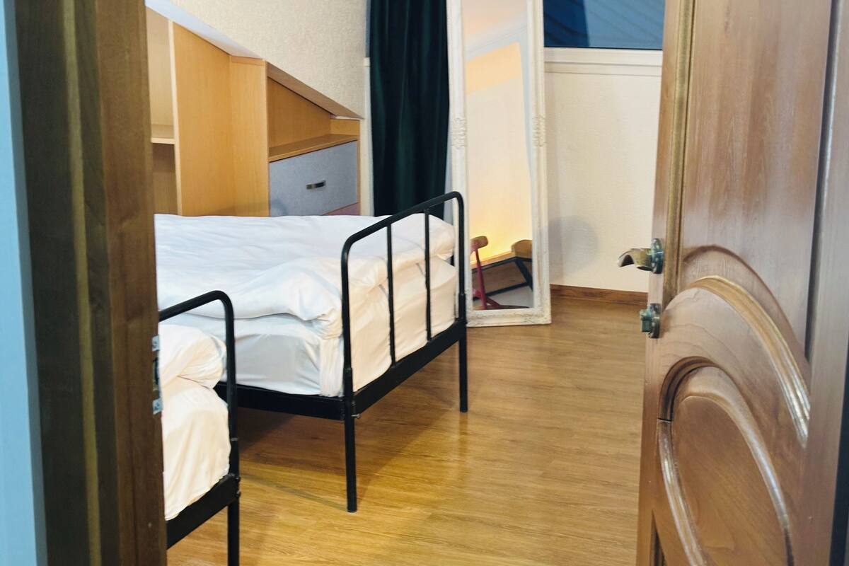 A small, narrow room with a bunk bed, a wooden cabinet, and a door.