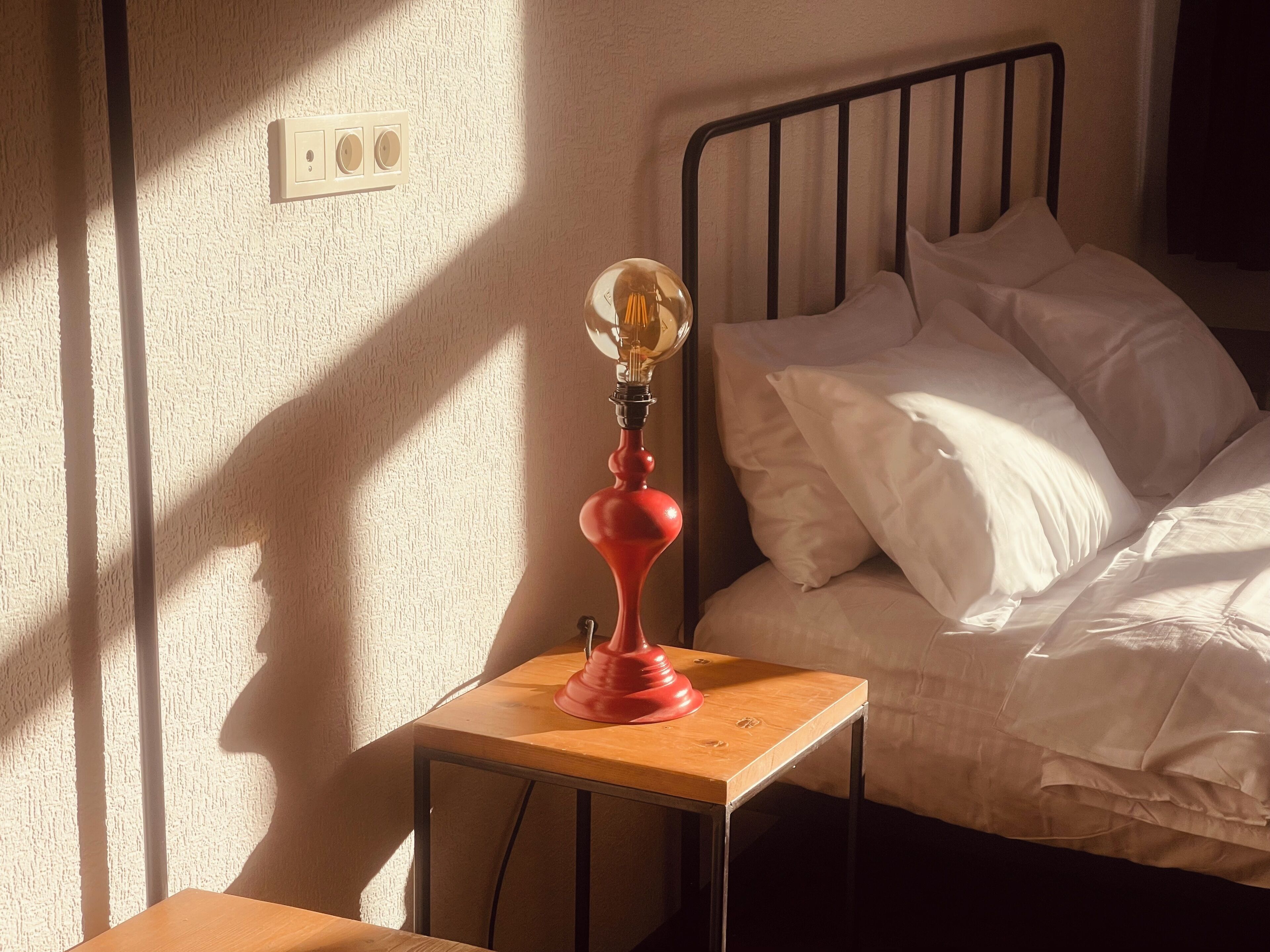 A bedroom with a bed, a bedside table with a lamp, and a wall socket.
