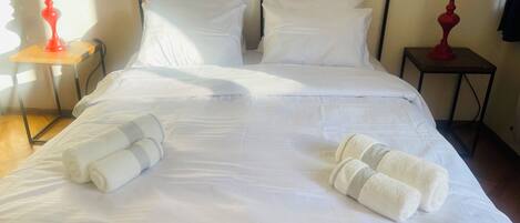 A neatly made bed with white linens and two rolled towels on the bed.