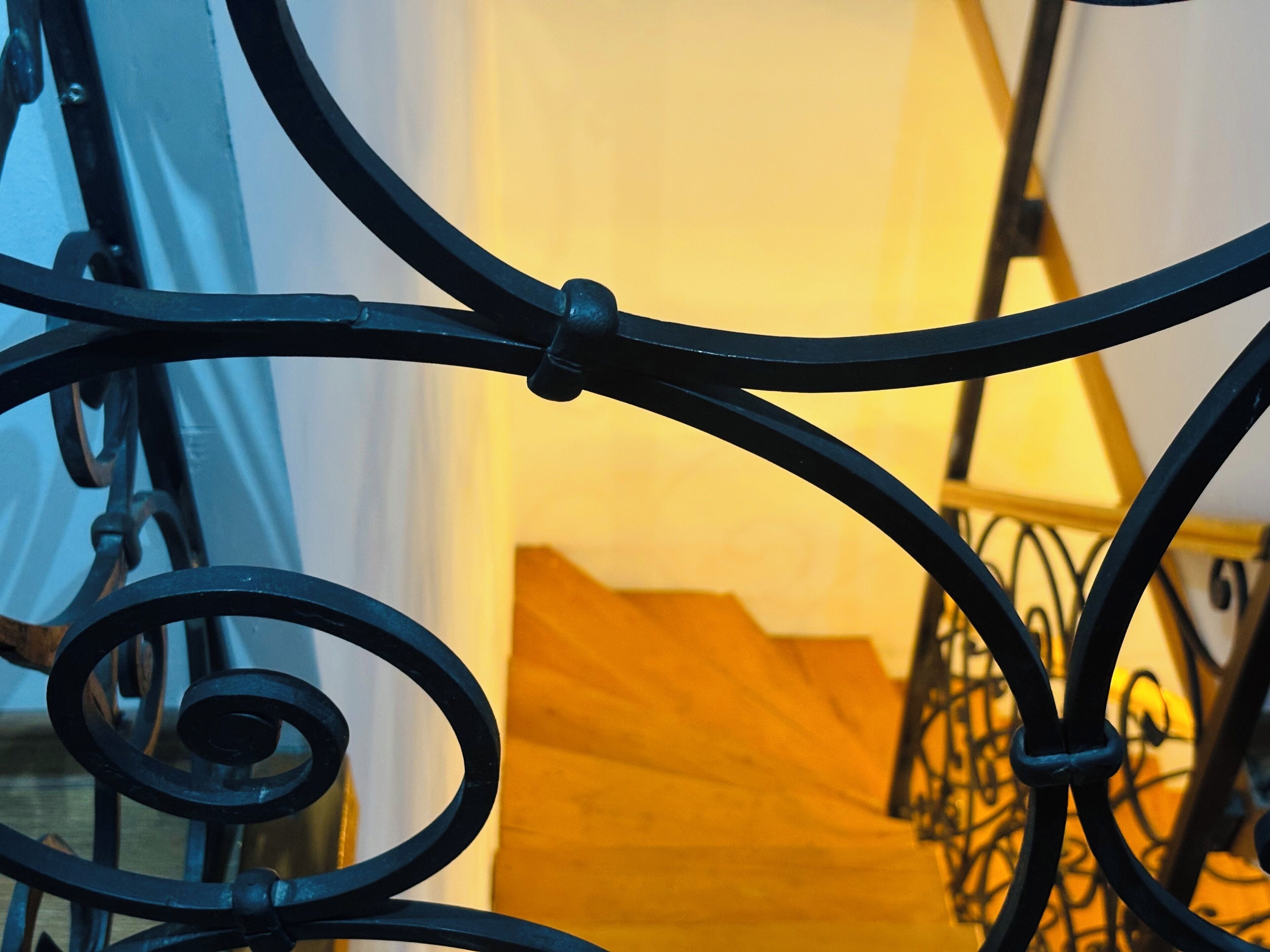 A staircase with a wooden finish and a metal railing with intricate designs.