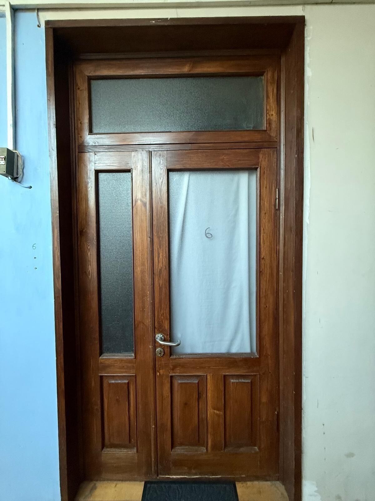 Een houten dubbele deur met een ruit en een deurklink.
