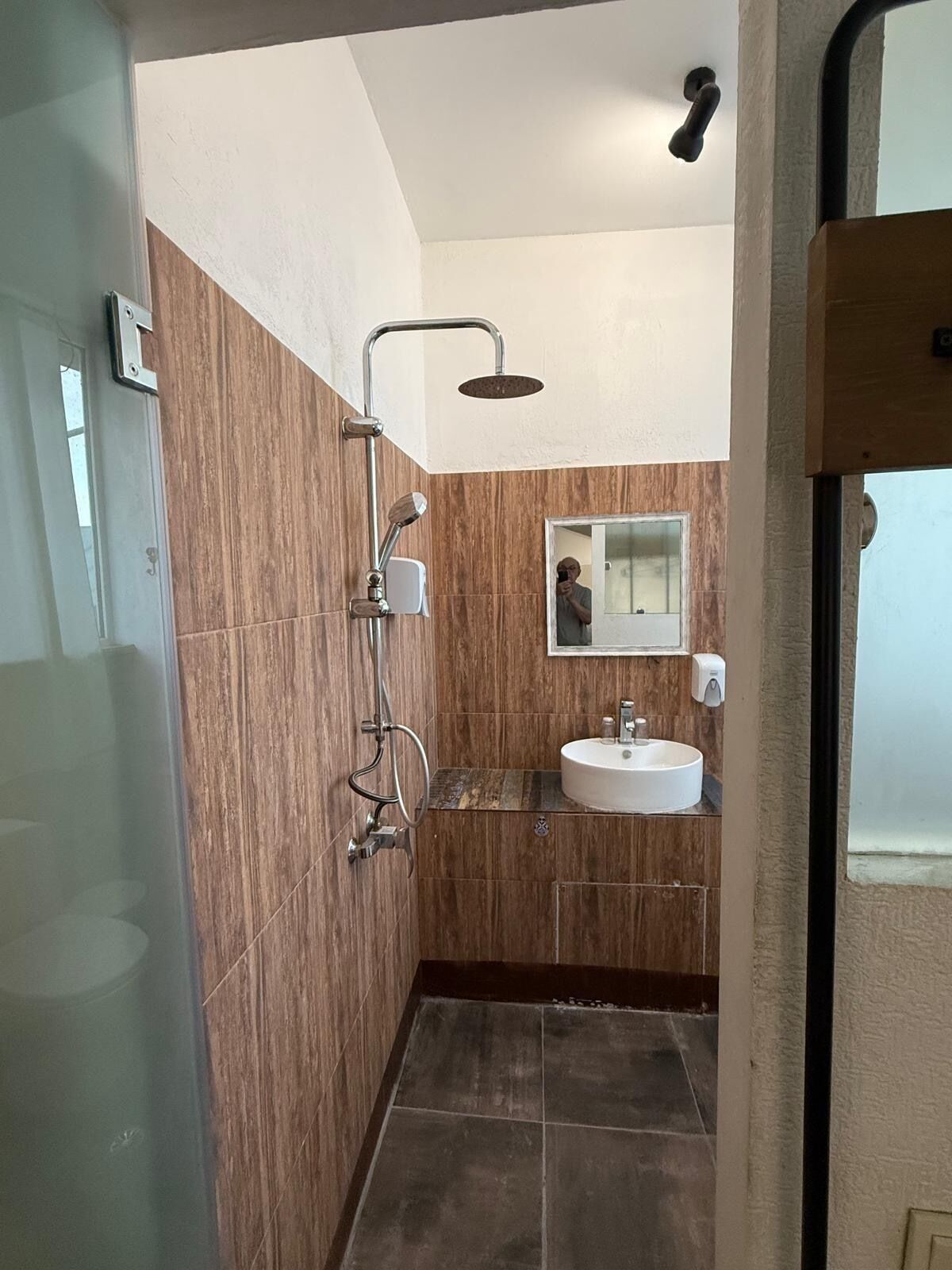 A modern bathroom with a wooden wall, a shower, a sink, and a mirror.