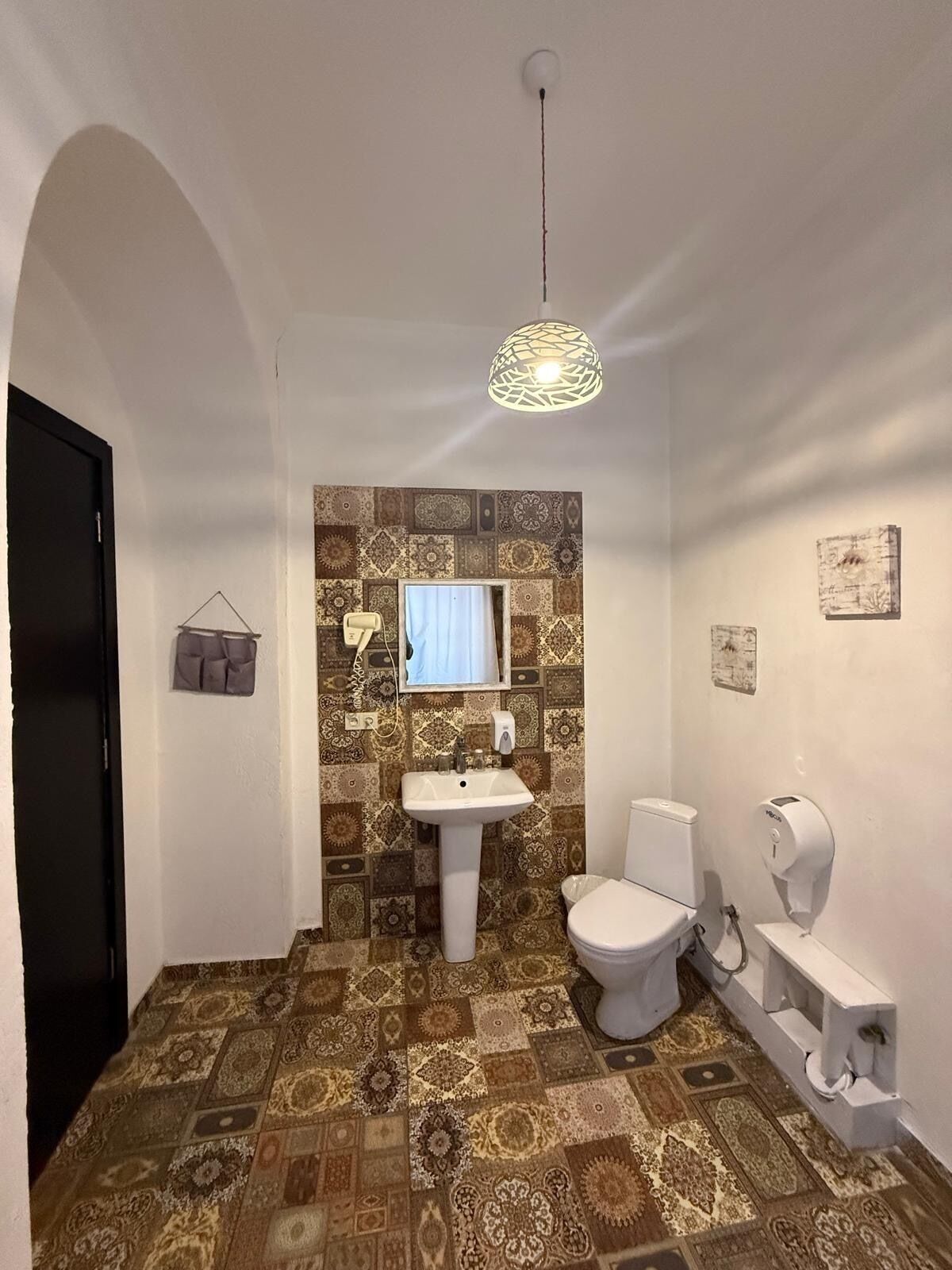 A bathroom with a patterned floor, a sink, a toilet, and a hanging light fixture.