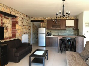 Un espacio habitable compacto con una pared de piedra, una kitchenette, una zona de comedor con taburetes y un sofá.