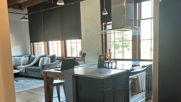 Een ruime keuken met een groot eiland, houten balken in het plafond en een uitzicht op de omgeving door grote ramen.