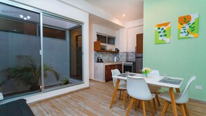 A modern kitchen with a dining area, a sliding glass door leading to a balcony, and a green wall with two abstract paintings. - Charming 2-bedroom condo in Tulum with WiFi, AC (Tulum)
