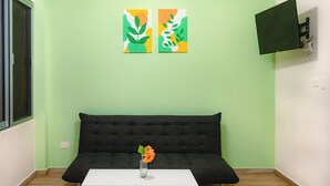 A room with a green wall, a black sofa, a white coffee table with a vase of flowers, and two abstract paintings. - Charming 2-bedroom condo in Tulum with WiFi, AC (Tulum)