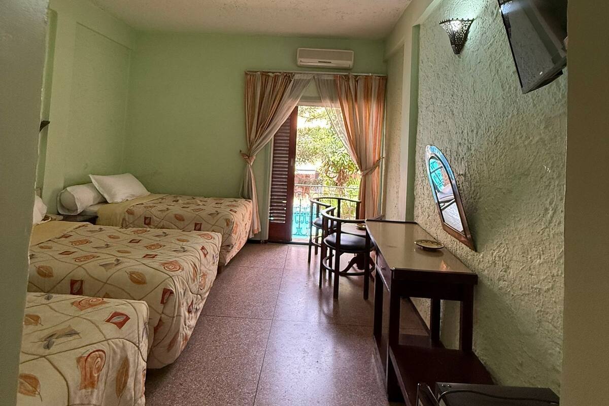 Ein Hotelzimmer mit zwei Betten, einem Esstisch, Stühlen, einem Fernseher und einer Klimaanlage.