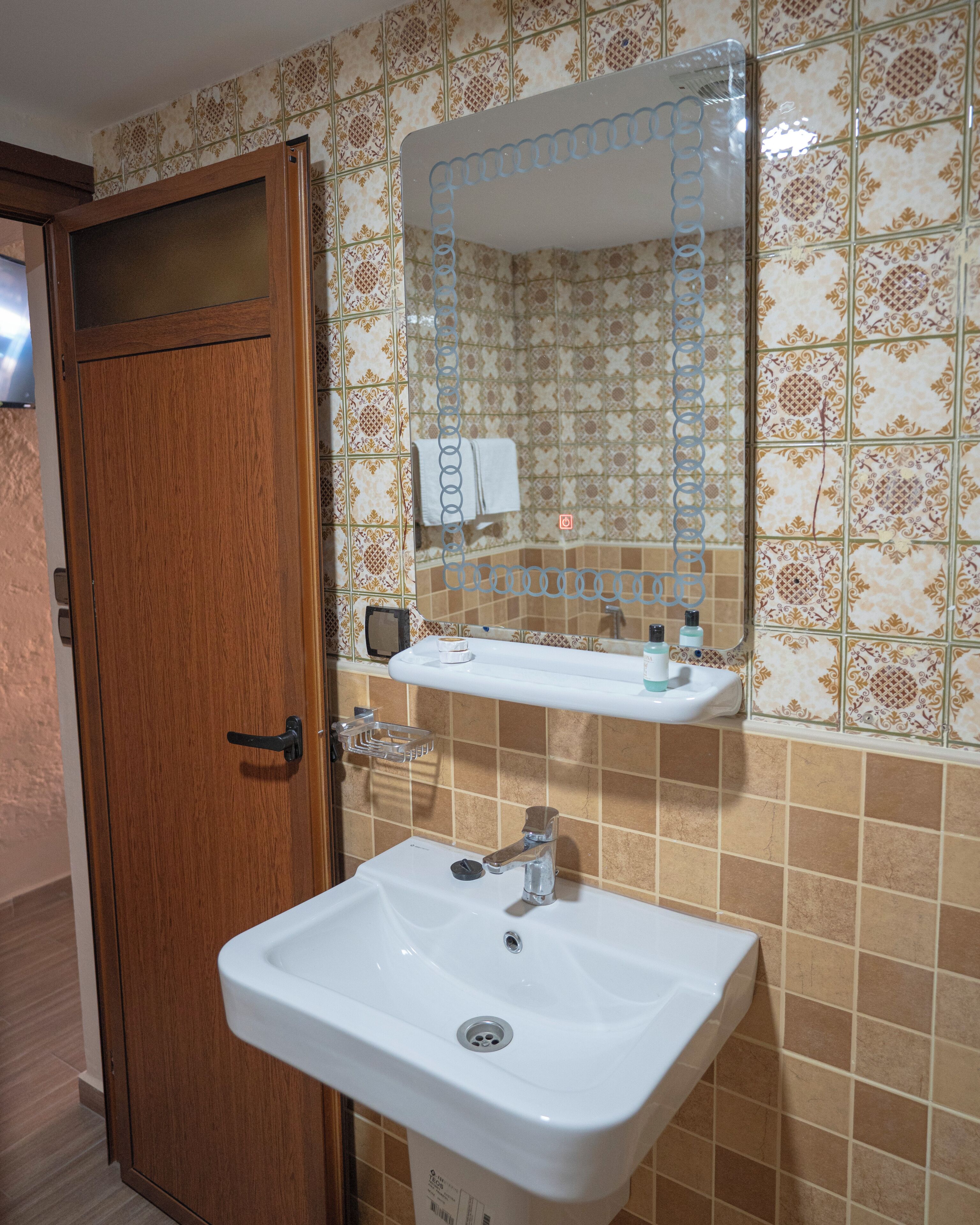 Een badkamer met een houten deur, een wit wastafelmeubel, een spiegel en betegelde vloeren.