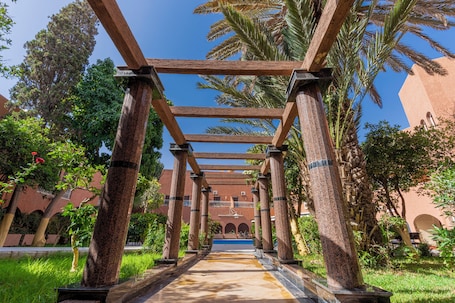 Un couloir bordé de colonnes, une piscine et, au fond, un bâtiment orné d’arches.. Tiznit Hotel
